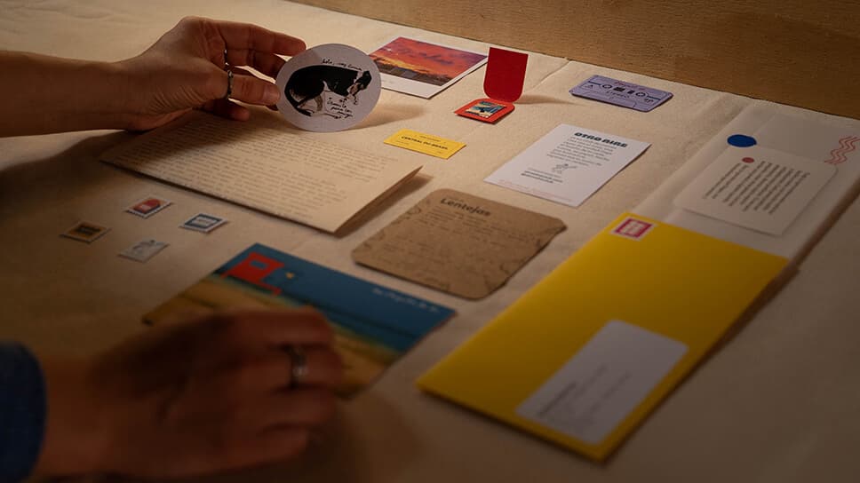Los artefactos gráficos de una carta desplegados sobre una mesa: calcos, estampillas, postales, una ficha de receta y el sobre amarillo